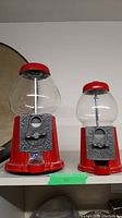 Two red vintage Continental Gum of Canada gumball machines side-by-side, showing size difference, coin slot plates, and glass globes.