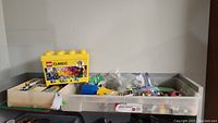 Two plastic storage bins filled with assorted LEGO Classic pieces including bricks, plates, and some specialties. One bin has a yellow LEGO Classic box on top.
