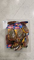 Photo showing a large plastic bin filled with multiple unopened packages of marbles, labeled as 81 marbles per pack, some packages piled on top of each other.