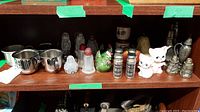 Shelf with assorted salt and pepper shakers and children’s cups in various materials and designs