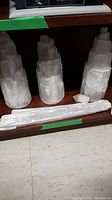 Three large white salt crystal blocks shaped like towers and one long white crystal stick on a wooden shelf.