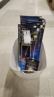 White storage basket containing 13 star swords in black rectangular packages and one mood ring in black packaging.
