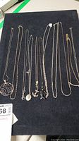 Top view of all ten silver necklaces laid out on black surface.