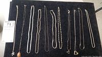 Top view showing all eleven necklaces laid out on a black velvet surface, displaying variety of pendants and chain styles.