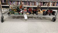 Wide view of vintage Tonka trucks and tractors, candle powered boats, and John Deere card set on metal shelf with books in background.