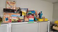 Full lot of vintage games including boxed board and table games stacked on white table.