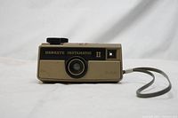 Front view of Kodak Hawkeye Instamatic II camera showing lens, viewfinder, and wrist strap