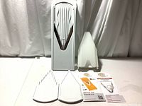 Front view of the slicer body, three blade inserts, safety guard, and instruction materials.