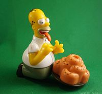 Front view showing Homer Simpson kneeling with tongue out towards doughnuts.