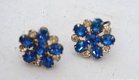 Close-up photo showing the pair of vintage clip-on earrings with blue and clear rhinestones in a round cluster arrangement on silver-tone metal.