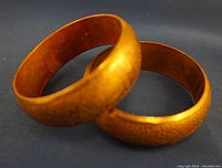Two brass hand hammered bracelets showing outer floral engraved pattern on dark blue fabric background.