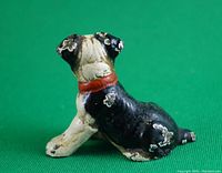 Side view showing the dog sitting pose, black and white paint with red collar, some paint chipping on back and tail areas.