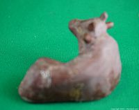 Top and side view of a miniature pottery resting cow figurine on a green background showing wear and brown coloring.