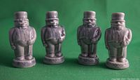 Front view of four small ceramic figures of men with top hats and suits on a green surface.