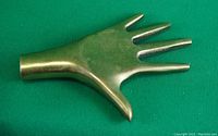 Solid brass left hand miniature lying on green fabric, showing the top and detail of fingers and thumb.