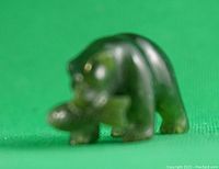 Front angle of green jade bear figurine holding a fish, showing shape and carving details.