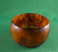 Front view of amber tortoise shell Bakelite bangle bracelet on green background.