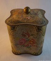Front and top view of vintage square floral tin showing floral motifs, scalloped lid, and brass knob.