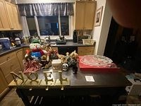 Overview of all Christmas decorative items arranged on a kitchen counter including Mikasa platter, Noel stocking hangers, plush snowman, dolls, and other holiday decorations