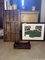 Photo showing antique wood printer's tray, vintage framed print signed by artist, and vintage card catalog tray with yellow cabinet behind.