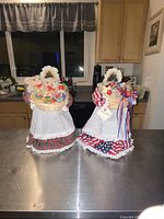 Front view showing both Apple Annie folk art apple head dolls on counter, highlighting Christmas and patriotic themes