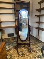 Front view of wooden framed full length oval mirror on swivel base in room with patterned tile floor.