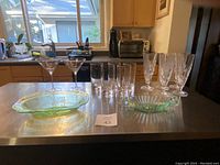 Kitchen countertop with two uranium glass oval dishes, two etched martini glasses, four Princess House pilsner glasses, and four plain tumblers arranged.