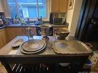 Photo showing entire collection of various silver plated serving pieces on a table including tray, bowl, bucket, platters, and coffee pot.