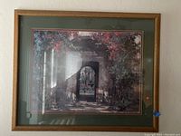 Front view of the large print in a heavy wood frame showing the outdoor stone archway scene with greenery and flowers.