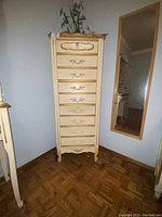 Full view of tall narrow cream colored lingerie dresser with gold accents and eight drawers.
