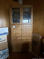 Full view of the tall wood Mid-Century Modern display cabinet showing all doors and drawers closed with visible wood grain and glass doors at top section