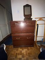 Front view of wooden shoe cabinet with two closed compartments and small attached wooden mirror on top.