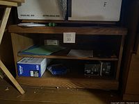 Front view of the wooden stand showing two lower shelves with various papers and small boxed items (not included in sale). Wooden finish is visible with some wear.