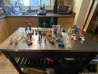 Overview photo of all toys and action figures on a kitchen counter, showing variety of figures including dinosaur-themed ones, humanoid figures and toy cars