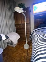 Full view of the generic standing lamp in a bedroom showing base, pole, flexible neck, and light fixture.