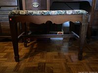 Side view of upholstered wooden bench showing floral fabric seat and scuffed wood frame.
