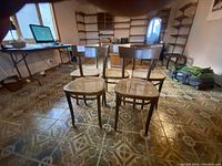 Five vintage solid wood dining chairs with cane seats arranged in a room, showing front and side angles.