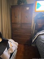 Full view of vintage wooden armoire showing overall condition and size compared to nearby bed and window.
