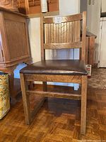 Front view of the solid wood chair showing the vinyl seat and slatted wood backrest.