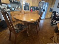 View of dining table with four matching chairs in kitchen setting, showing oval wood table with pedestal legs and upholstered chairs.