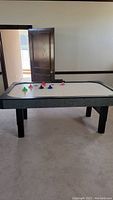 Full view of air hockey table indoors with paddles and pucks on table.