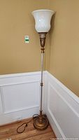 Full view of the antique brass floor lamp with opaque glass globe shade and visible cord on hardwood floor