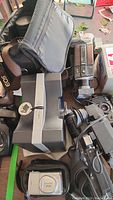Photo showing Canon cameras, vintage video recorder, a camera lens, and a soft camera carrying bag packed together.
