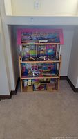 Full view of the wooden doll house showing three stories and colorful interior design