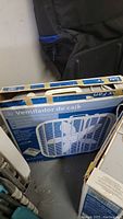 Two boxed GAL box fans stacked and stored upright, showing front of the packaging and brand markings.