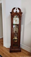 Full view of tall Sligh grandfather clock showing wooden case, bonnet top, and glass door.