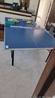 Full view of the assembled blue ping pong table with paddles, net, and balls on top.
