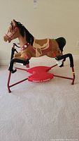 Front and side view of molded plastic rocking horse on red metal rocker frame showing horse details, saddle, bridle, and padded rocking arms.