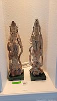 Two Asian carved statues shown side by side on green bases, visible wear and damage, 21 inches tall
