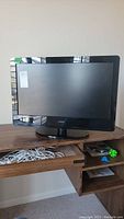 Front view of VIZIO 25-inch television on wooden surface, with visible cables in drawer below
